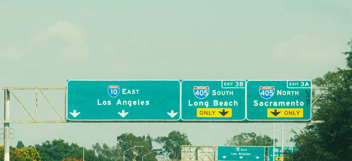 Highway signs with directions to Los Angeles, Long Beach, and Sacramento on a clear day.