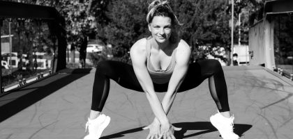 Woman in sports attire doing a crouching stretch on a bridge, black and white photo.
